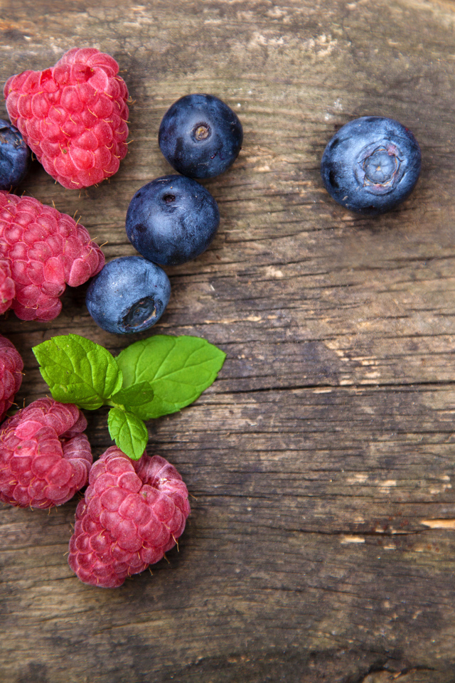 Голубые ягоды черники и красные ягоды малины на деревянном столе