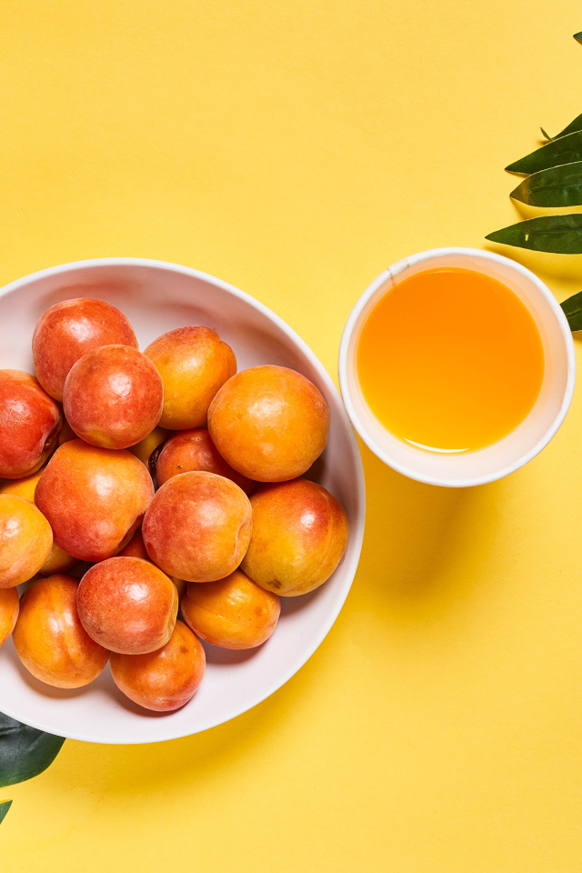 Вкусные спелые абрикосы с зелеными листьями на желтом фоне