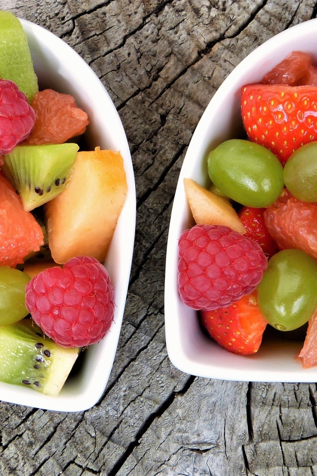 Салат из фруктов и ягод в белой тарелке на деревянном столе