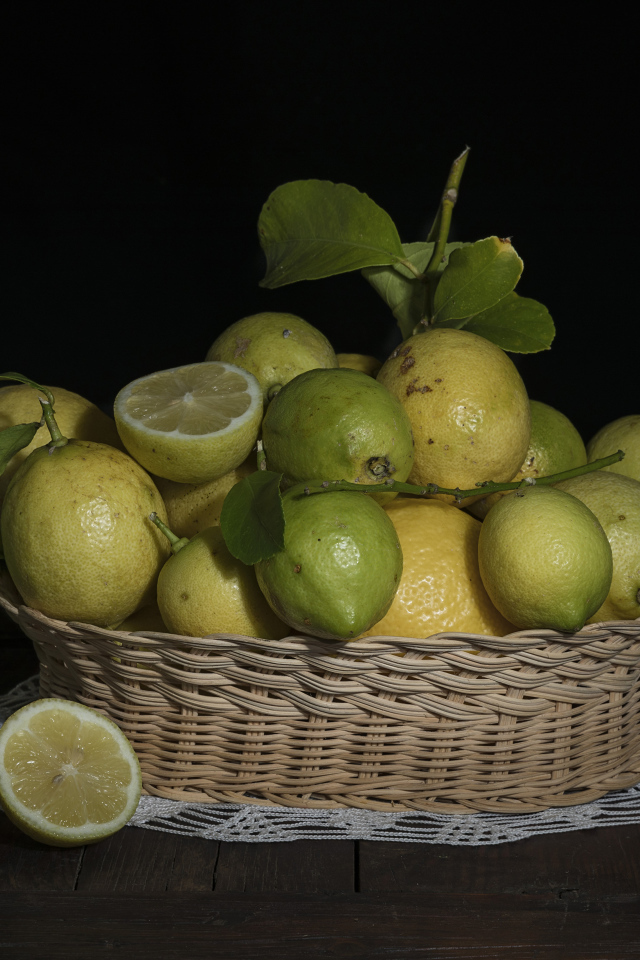 Lemons and limes in a wicker basket on a black background