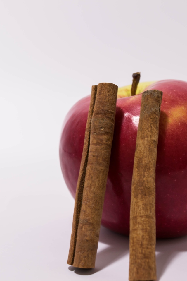 Красное яблоко с палочками корицы на сером фоне