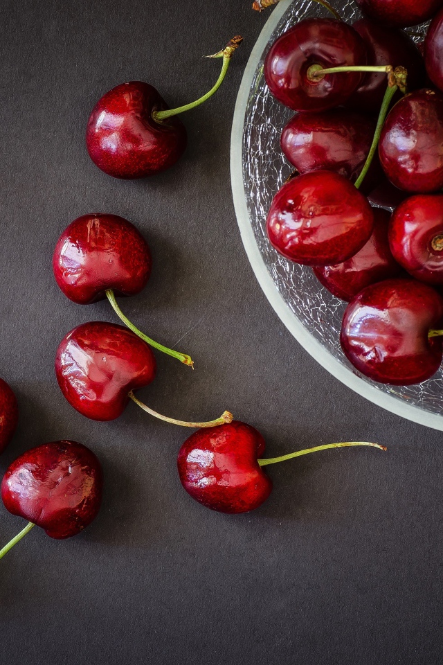 Красные черешни в миске на сером фоне