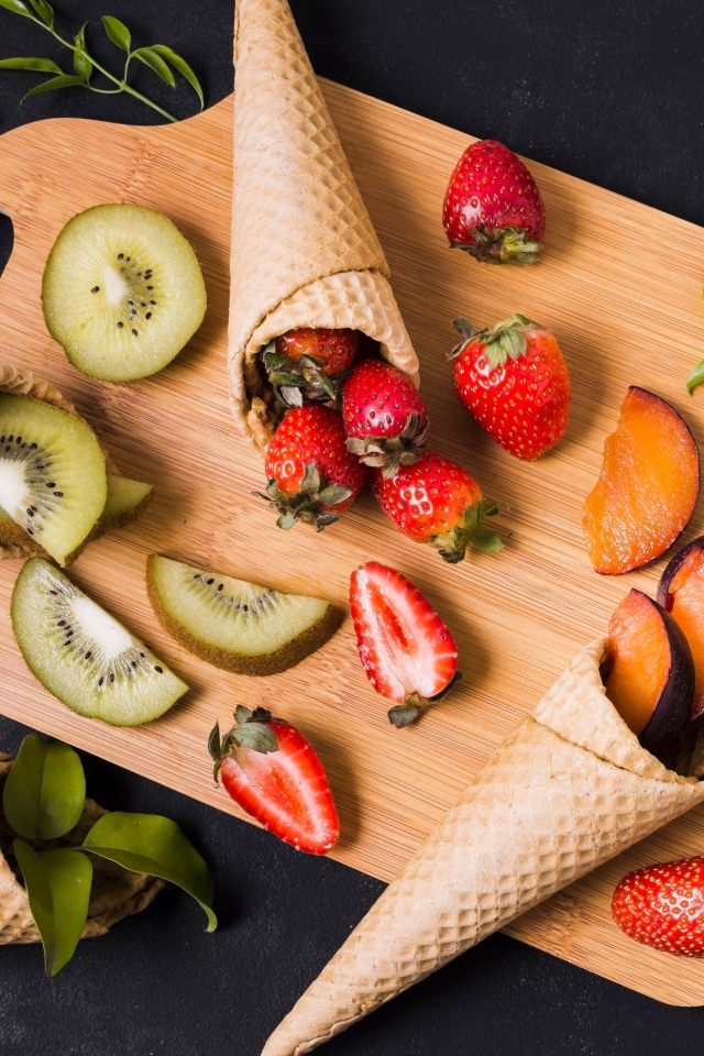 Вафельные рожки с ягодами и фруктами на доске 