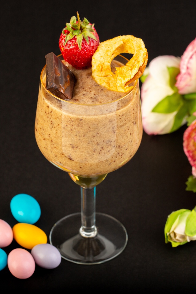 Коктейль с конфетами и букетом лютиков на черном столе