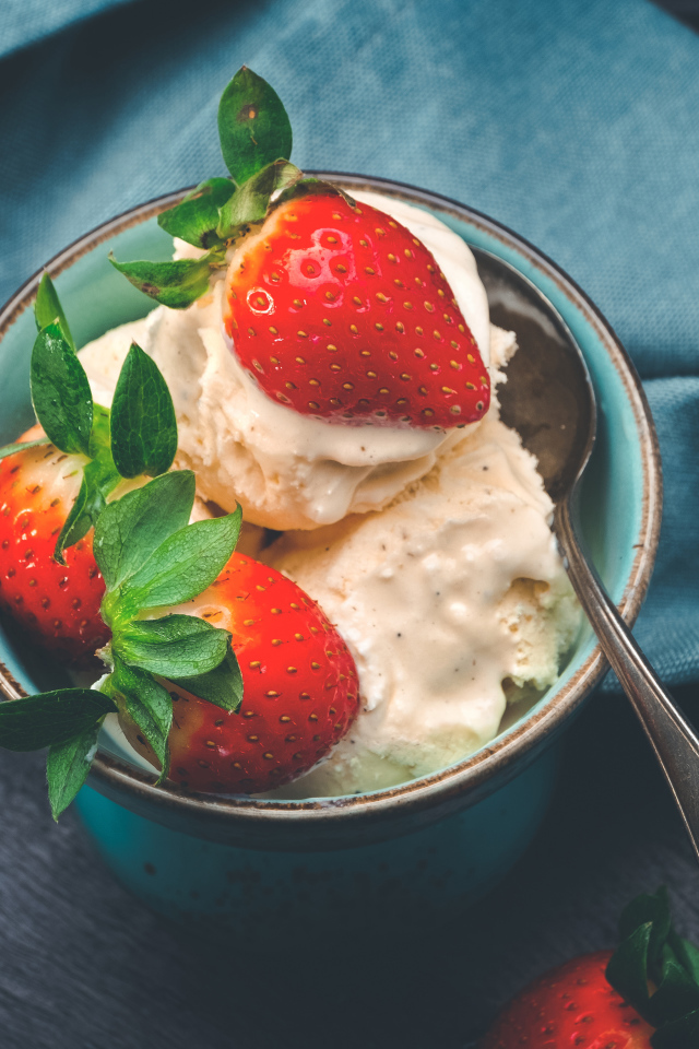 Сливочное мороженое с ягодами клубники в чашке с ложкой