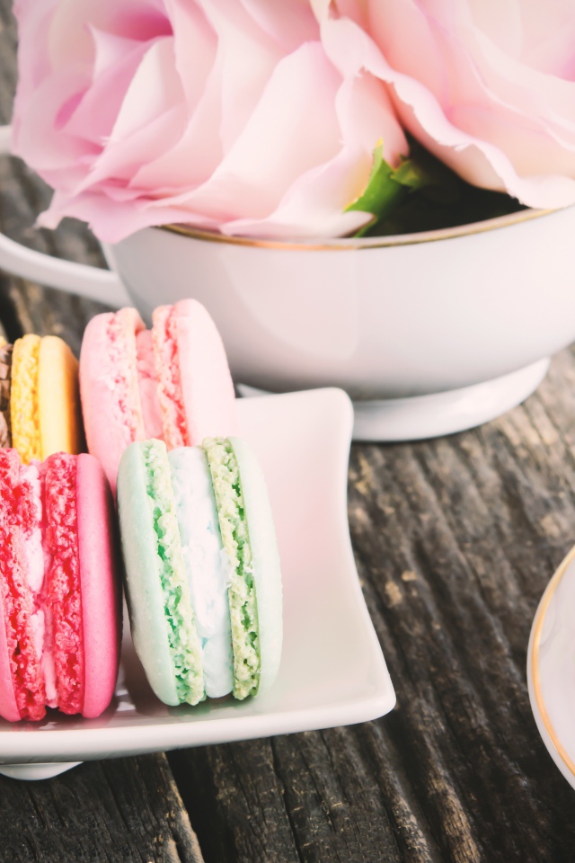 Десерт макарон на столе с чаем и цветами розы