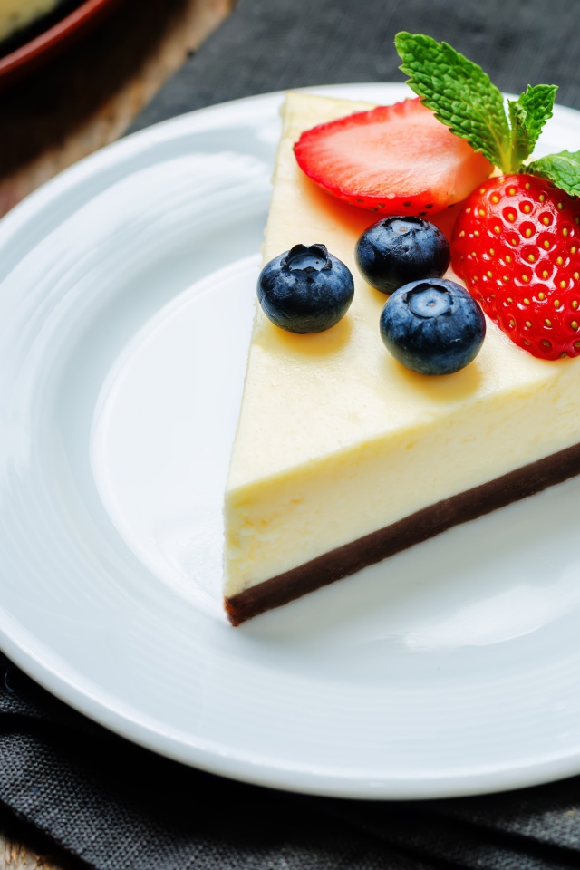 Кусок чизкейка на белой тарелке с клубникой и черникой 