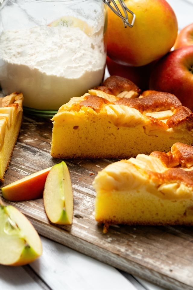 Куски пирога на столе с яблоками и мукой