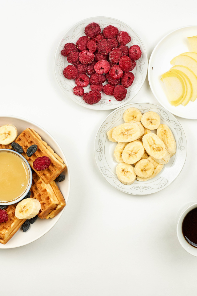 Сладкие вафли с малиной и бананами на столе  с кофе