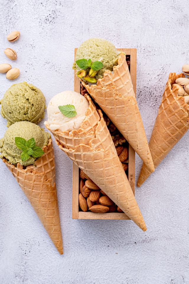 Вафельные рожки на столе с фисташковым мороженым и миндалем 