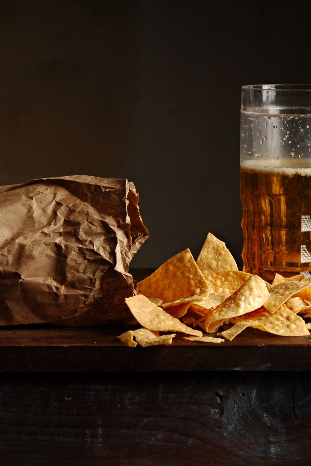 Бокал пива с чипсами в пакете на столе