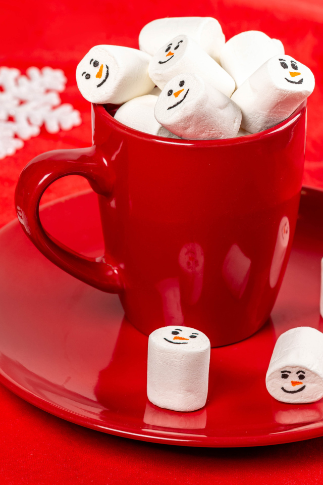Красная чашка с маршмеллоу на столе со снежинками