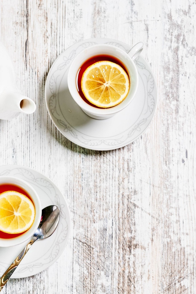 Две чашки чая с лимоном на столе с белым чайником