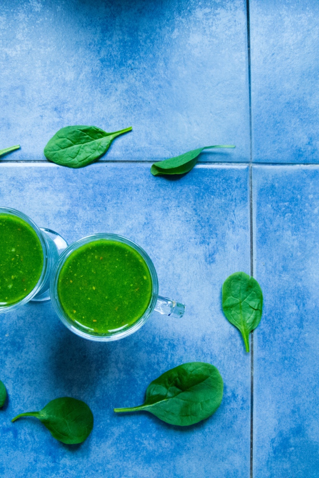 Два зеленых смузи с листьями базилика на голубом фоне