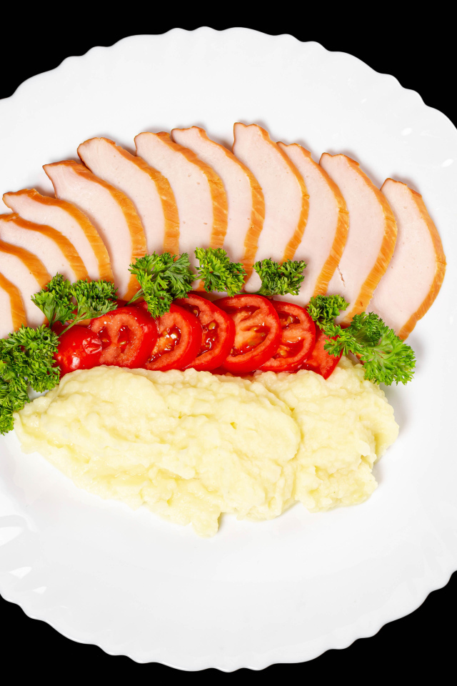 Ham on a large white plate with potatoes and tomatoes