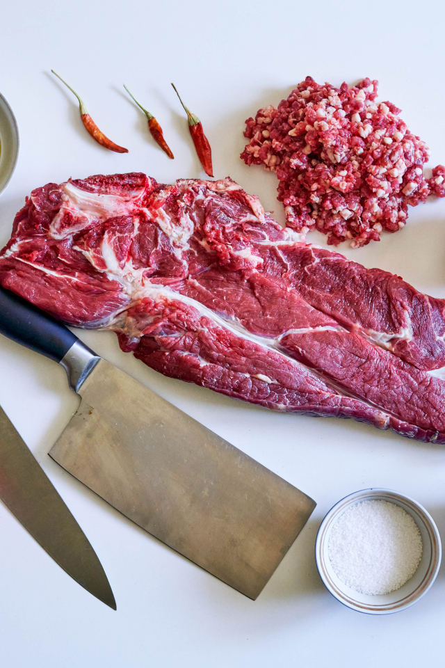 Кусок мяса со специями и ножами на столе 