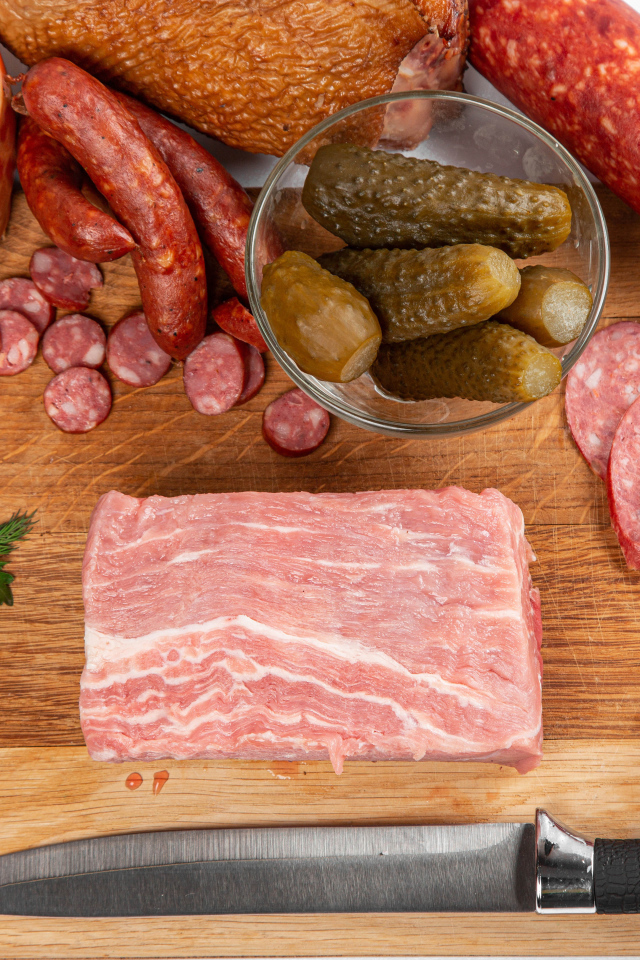 Колбаса на столе с огурцами, помидорами и зеленью 