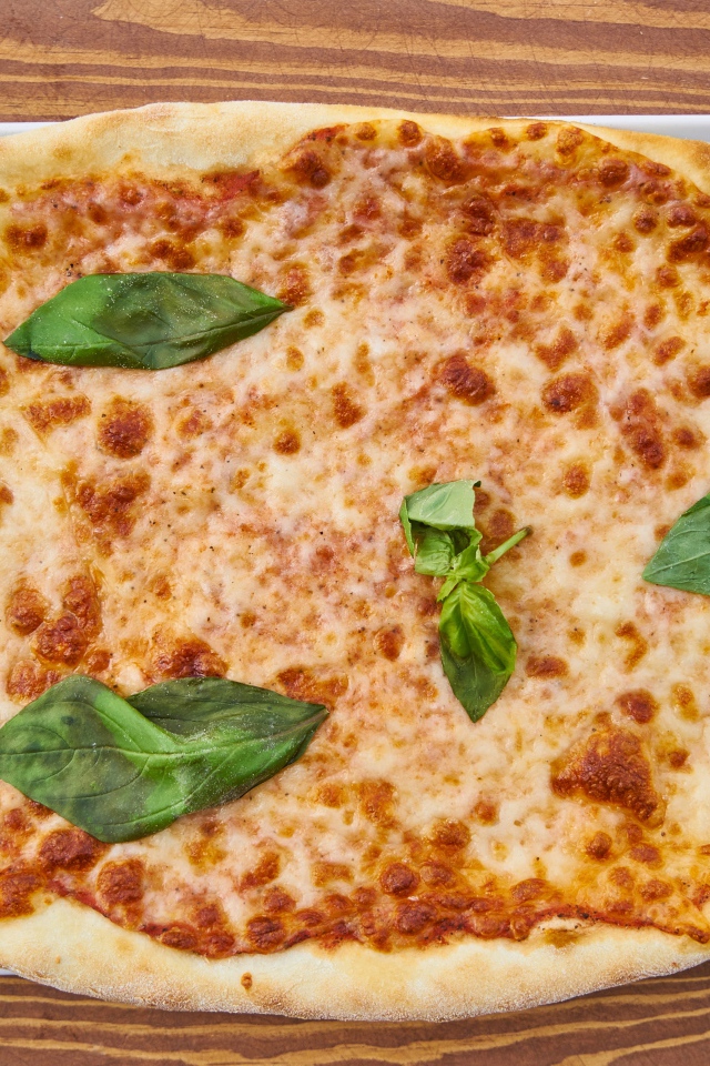 Пицца с сыром и листьями базилика на столе со столовыми приборами