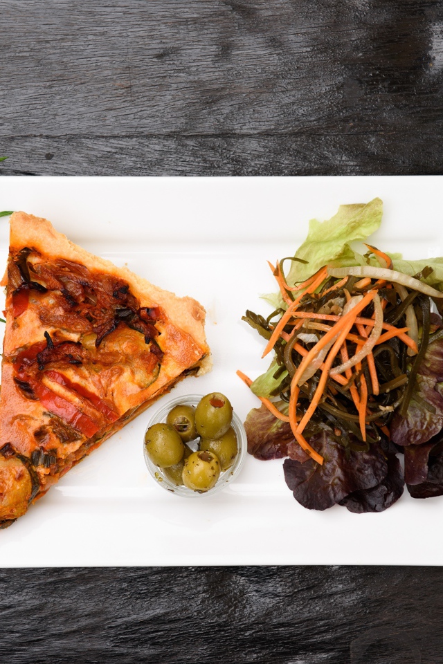 Кусок пиццы с салатом и оливками на белой тарелке