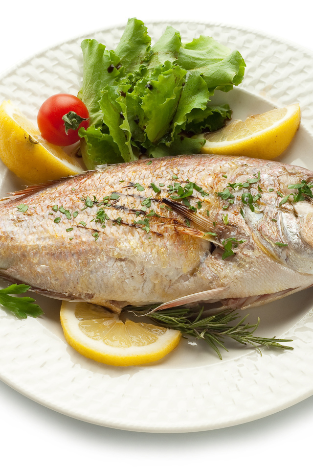 Baked fish on a plate with herbs and lemon