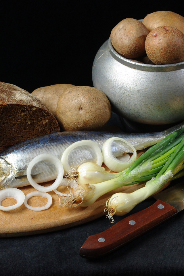 Сельдь на столе с картофелем, черным хлебом и луком 