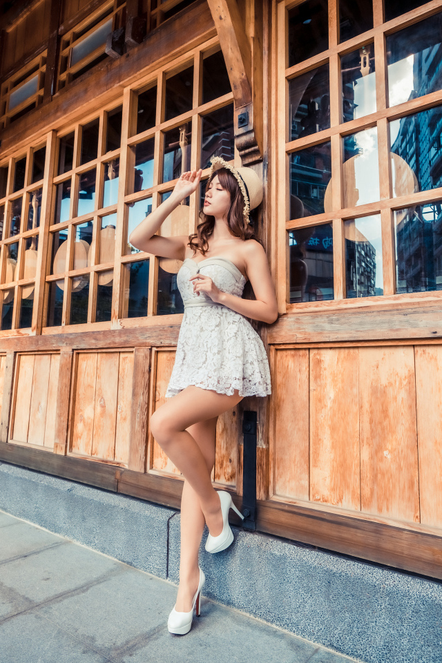 Красивая азиатка в платье стоит у окна кафе