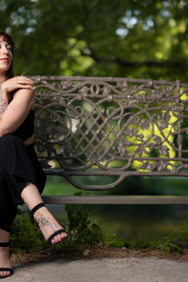 Девушка в черном костюме сидит на лавке 