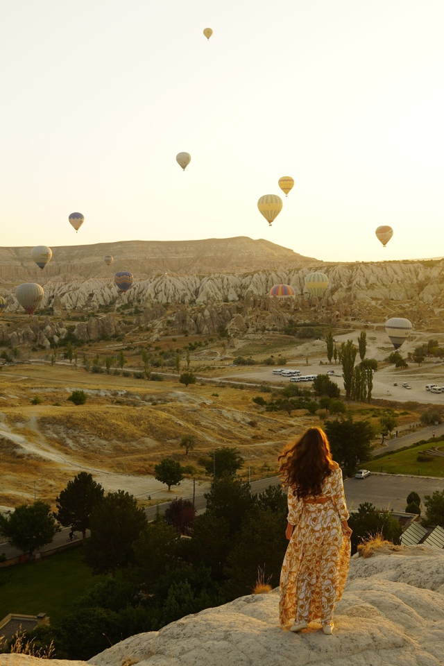Девушка стоит на краю скалы на фоне неба с воздушными шарами