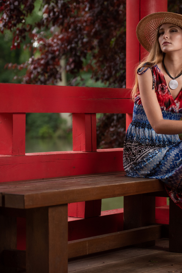 Молодая девушка в платье сидит на лавке 