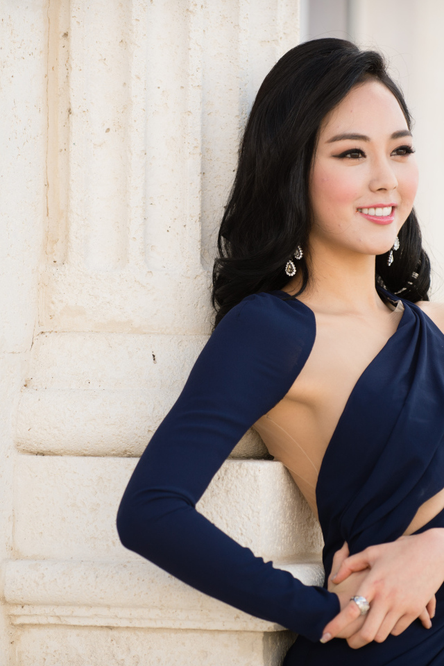 Молодая девушка в платье стоит у стены 