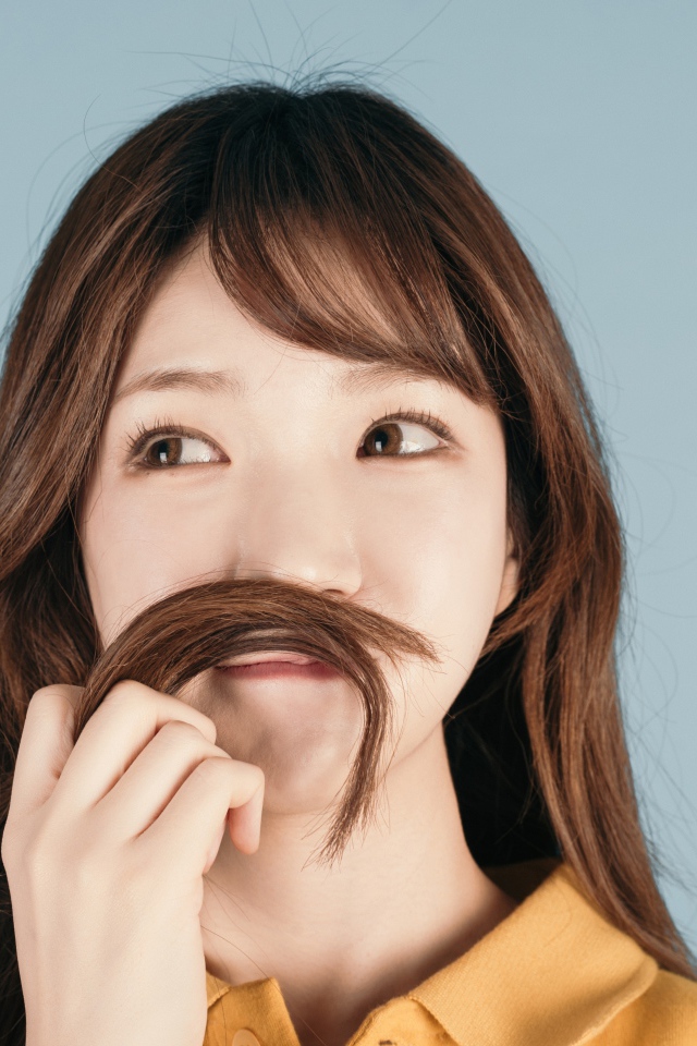 Девушка азиатка закрыла лицо волосами на сером фоне 