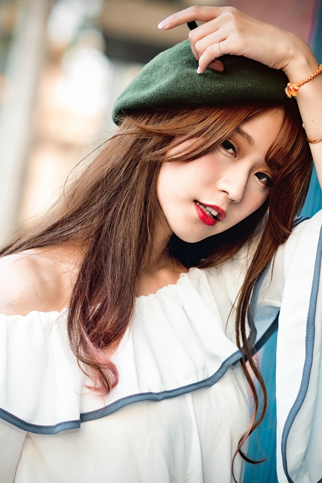 Девушка азиатка в берете стоит у стены 