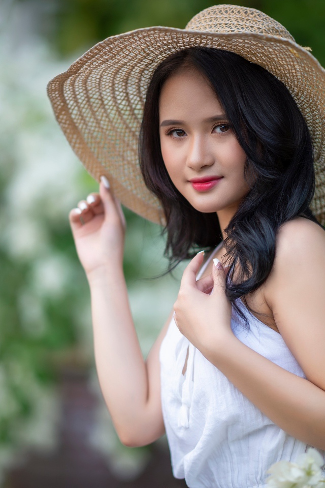 Девушка азиатка в большой шляпе у зеленого куста