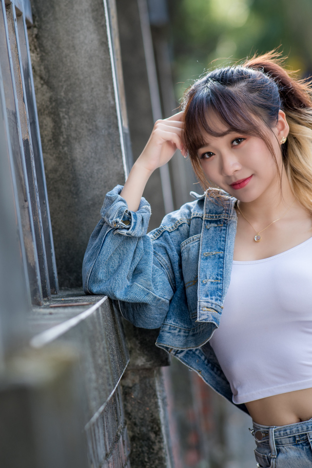 Девушка азиатка в джинсовой куртке у забора 