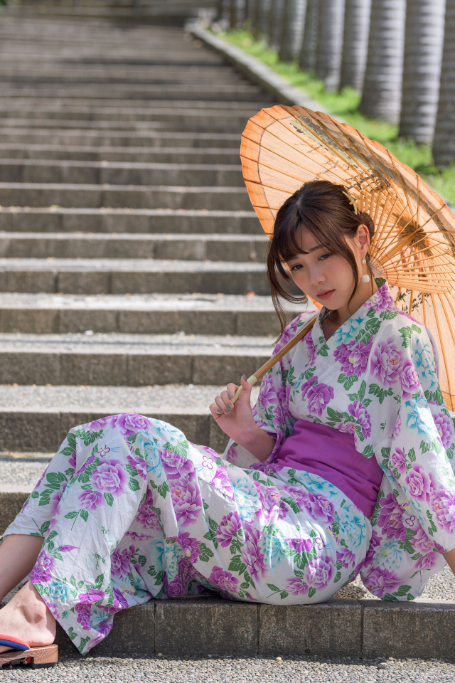 Девушка азиатка в кимоно с зонтом в руках сидит на ступеньках 