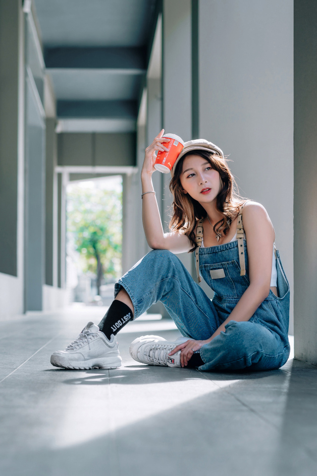 Девушка азиатка в синем комбинезоне с кофе в руке 