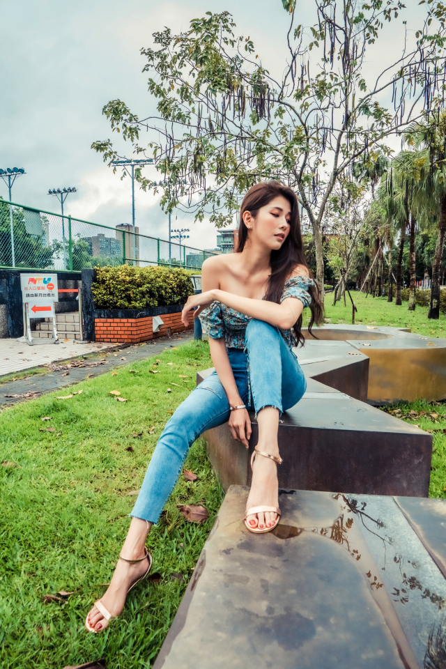 Девушка азиатка в джинсах сидит в парке 