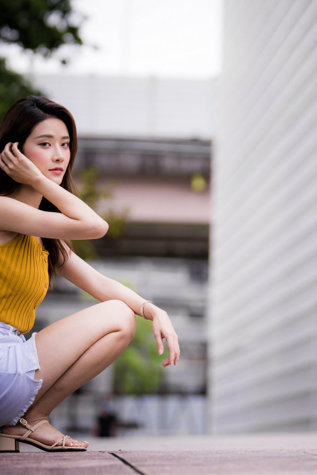 Девушка азиатка сидит на корточках у стены