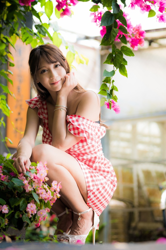 Девушка азиатка сидит на корточках у розового цветка