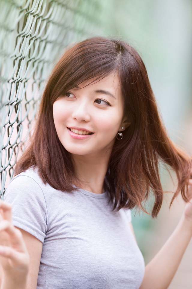 Девушка азиатка с милой улыбкой стоит у сетки 