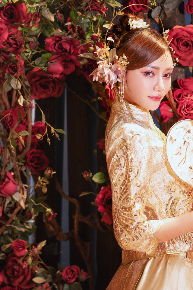 Азиатка в красивом национальном костюме у куста роз