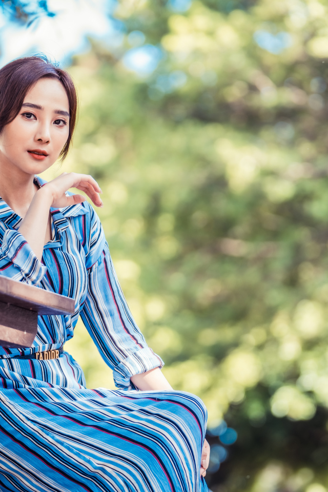 Красивая девушка азиатка в платье  за столом в парке 