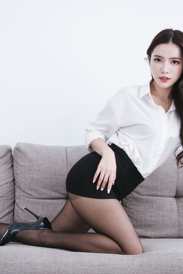 Красивая азиатка в белой рубашке на диване