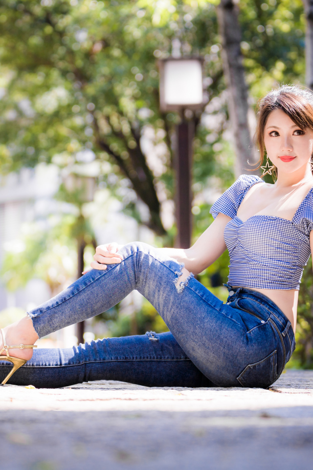 Красивая азиатка в джинсах сидит на земле