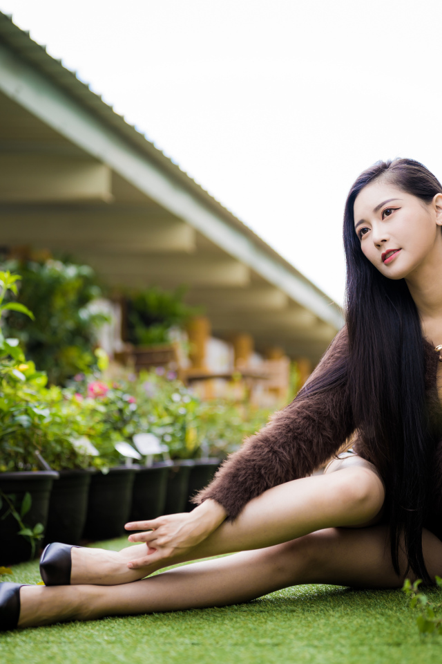 Красивая азиатка сидит на земле у цветов