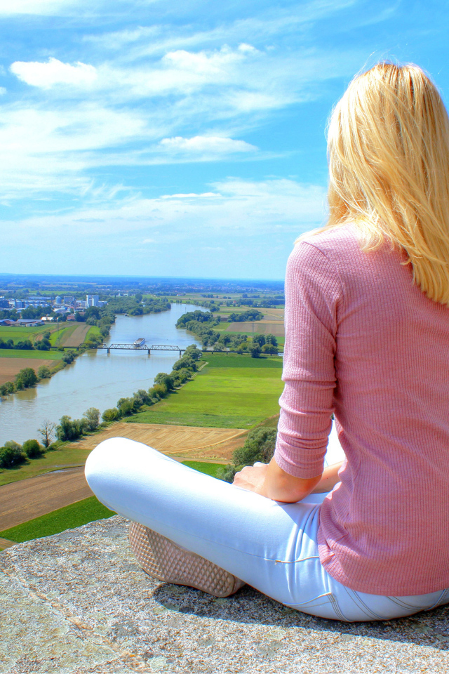 Красивая блондинка сидит на камне у реки