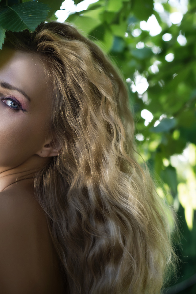 Красивая голубоглазая блондинка у ветки с зелеными листьями