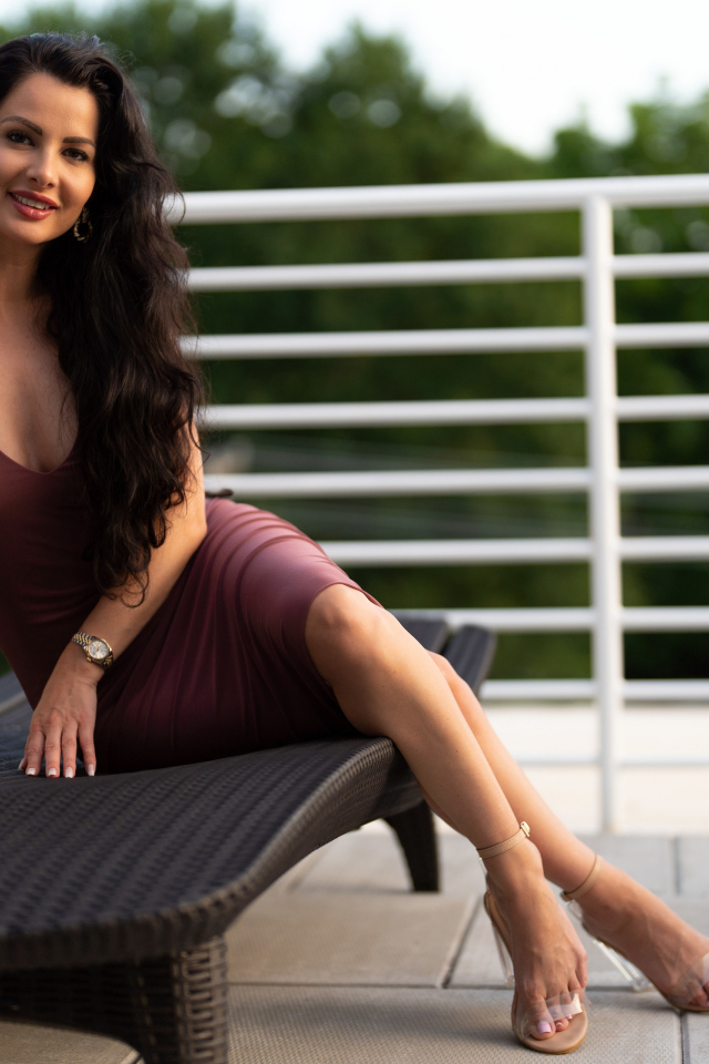 Красивая брюнетка в платье сидит на диване 