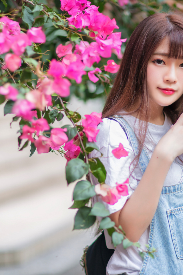 Красивая милая азиатка стоит у куста с розовыми цветами