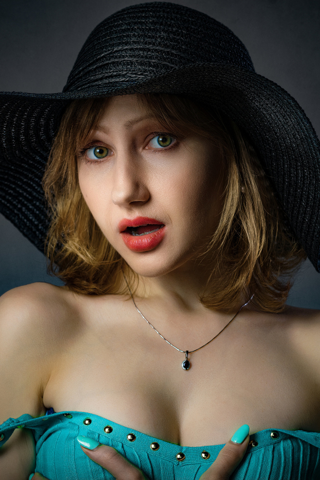 Красивая девушка в большой черной шляпе на сером фоне 